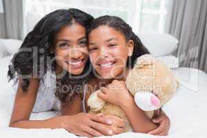 Pretty woman lying on bed with her daughter smiling at camera