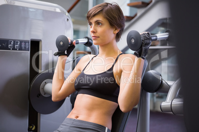 Smiling brunette using weights machine for arms