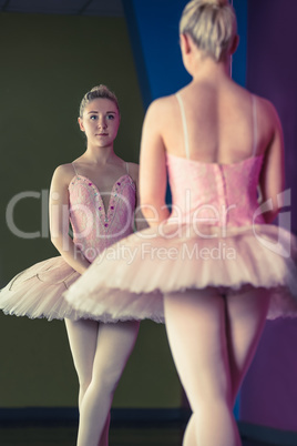 Graceful ballerina standing in first position in front of mirror