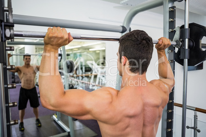 Shirtless muscular man lifting barbell in gym