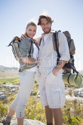 Hiking couple standing on mountain terrain smiling at camera