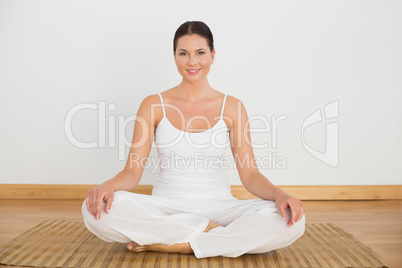 Smiling brunette sitting in lotus pose looking at camera