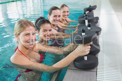 Female fitness class doing aqua aerobics with foam dumbbells