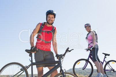 Fit cyclist couple standing at the summit smiling at camera