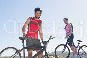 Fit cyclist couple standing at the summit smiling at camera
