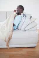 Sick man lying on sofa under a blanket