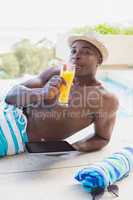 Handsome shirtless man using tablet pc poolside drinking cocktai