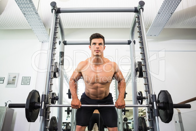 Shirtless muscular man lifting barbell in gym