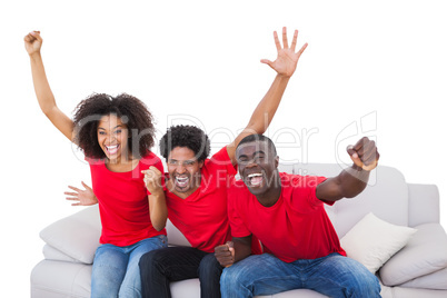 Football fans in red cheering on the sofa