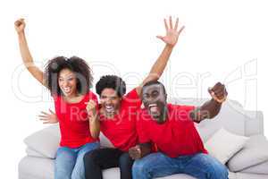 Football fans in red cheering on the sofa