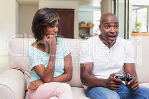 Bored woman sitting next to her boyfriend playing video games