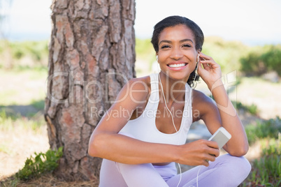 Fit woman sitting against tree listening to music