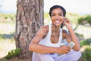 Fit woman sitting against tree listening to music