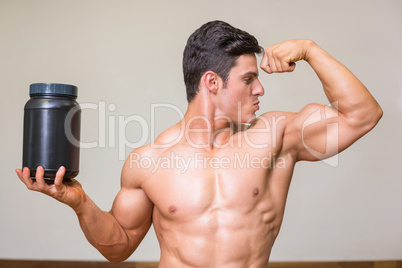 Muscular man posing with nutritional supplement in gym