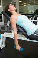 Fit brunette lifting dumbbells on bench