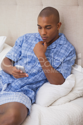 Thoughtful man sitting on bed sending text