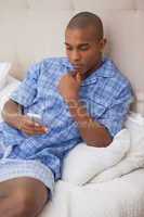 Thoughtful man sitting on bed sending text