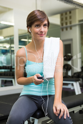 Fit brunette sitting on bench listening to music