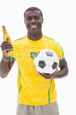 Happy brazilian football fan in yellow holding beer and ball