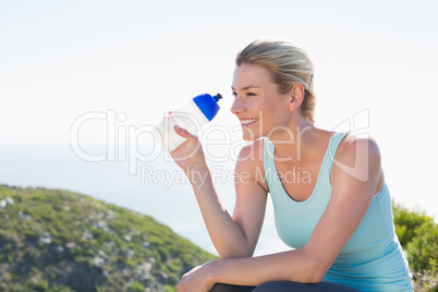 Fit blonde sitting at summit holding water bottle