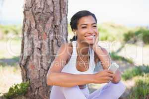 Fit woman sitting against tree listening to music