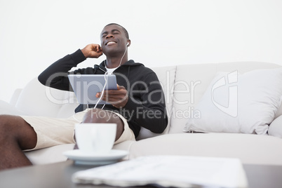 Casual man sitting on sofa enjoying music on his tablet pc