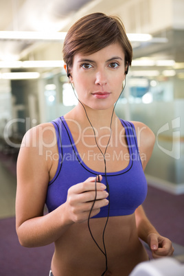 Fit brunette running on the treadmill listening to music