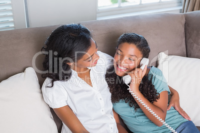 Happy mother and daughter on the phone together on sofa