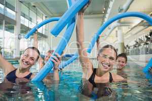 Happy fitness class doing aqua aerobics with foam rollers