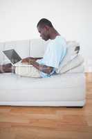 Casual man lying on sofa using laptop