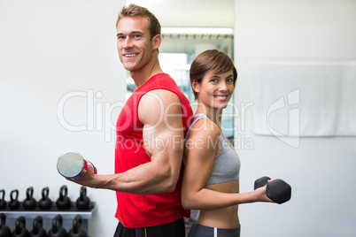 Fit couple lifting dumbbells together smiling at camera