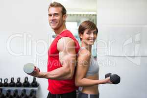 Fit couple lifting dumbbells together smiling at camera