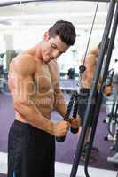Shirtless muscular man using triceps pull down in gym