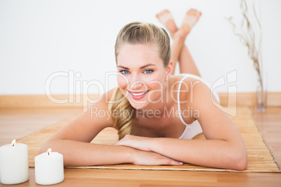 Peaceful blonde lying on bamboo mat smiling at camera