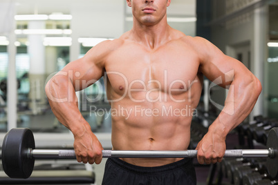 Mid section of a shirtless muscular man lifting barbell