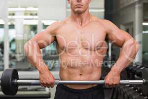 Mid section of a shirtless muscular man lifting barbell