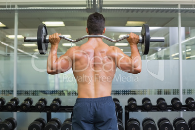 Rear view of a muscular man lifting barbell