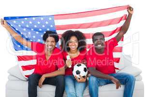 Happy football fans in red sitting on couch with usa flag