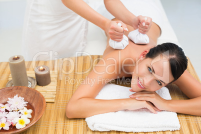 Peaceful brunette enjoying a herbal compress massage smiling at