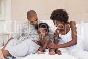 Happy couple sitting on bed with baby daughter