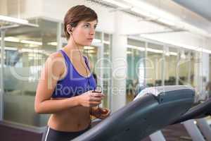 Fit brunette running on the treadmill listening to music