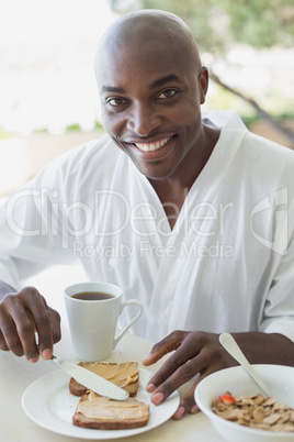 Handsome man in bathrobe having breakfast outside