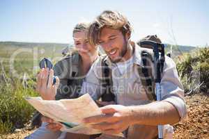 Hiking couple taking a break on mountain terrain using map and c