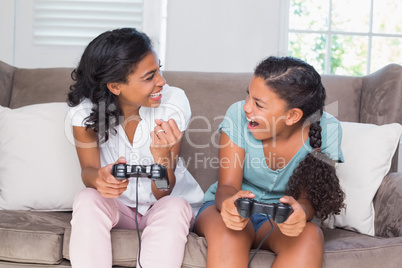 Happy mother and daughter playing video games together on sofa