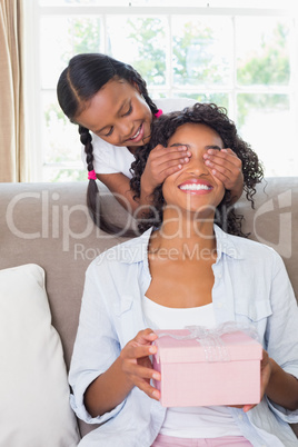 Pretty mother sitting holding gift with her daughter covering he