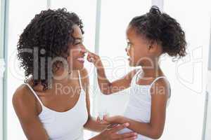 Cute daughter putting face cream on mothers nose