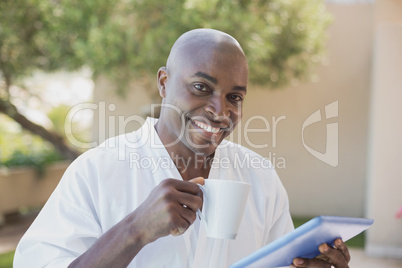 Handsome man in bathrobe using tablet at breakfast outside
