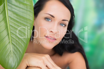 Beautiful nude brunette smiling at camera with green leaf