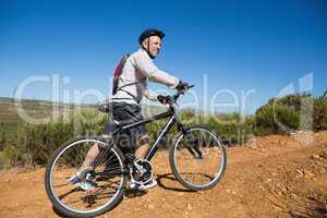 Fit cyclist pushing bike uphill on country terrain