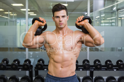 Muscular man lifting kettle bells in gym